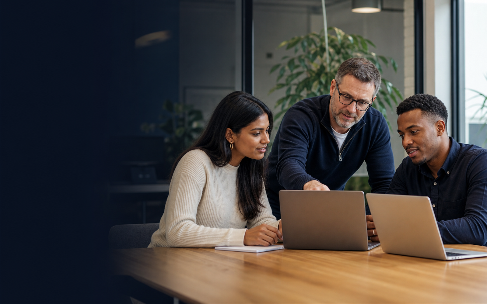 A workplace mentor and two adult learners collaborating around laptops